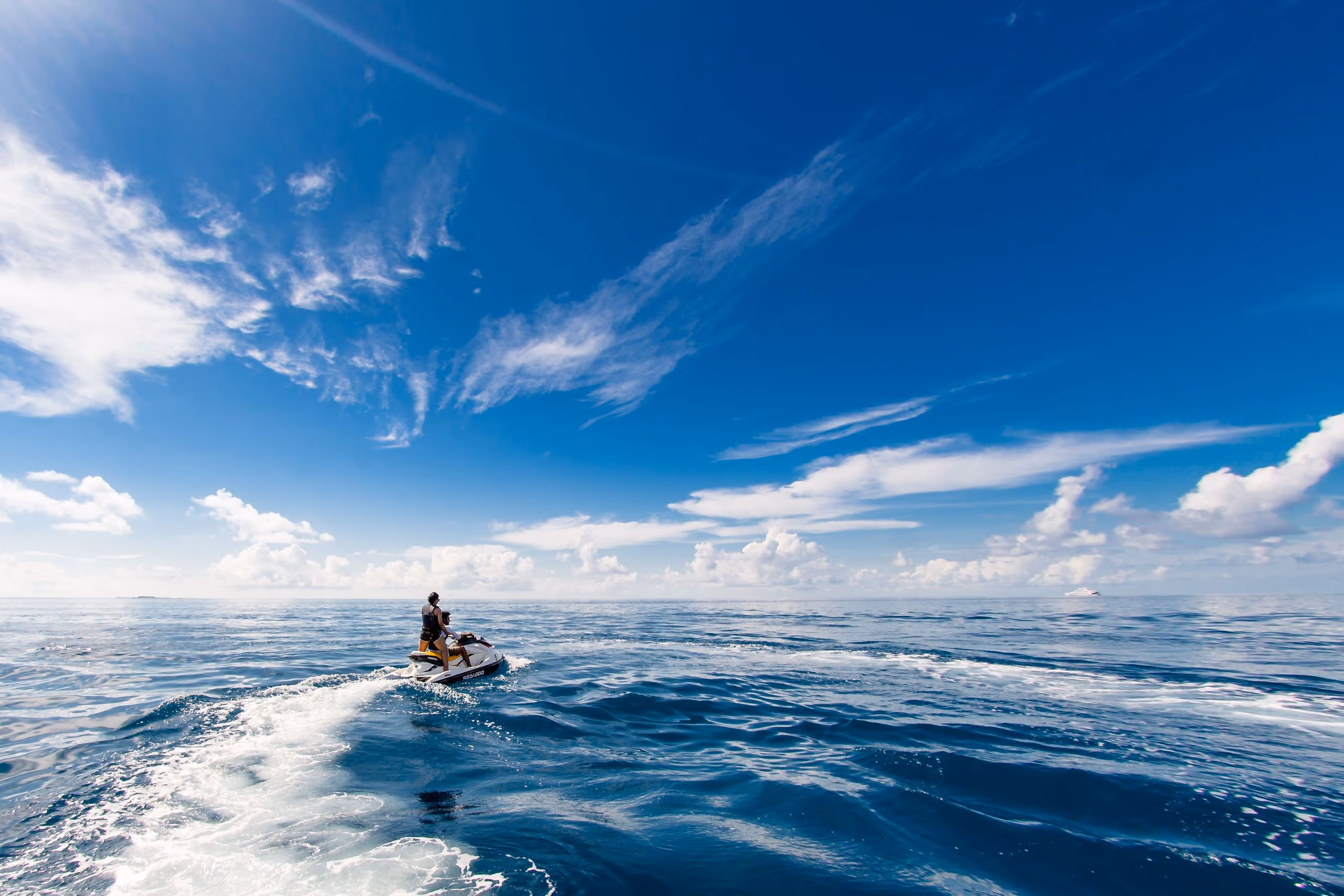 Jet Ski rider crossing deep blue open water, leaving a long white wake